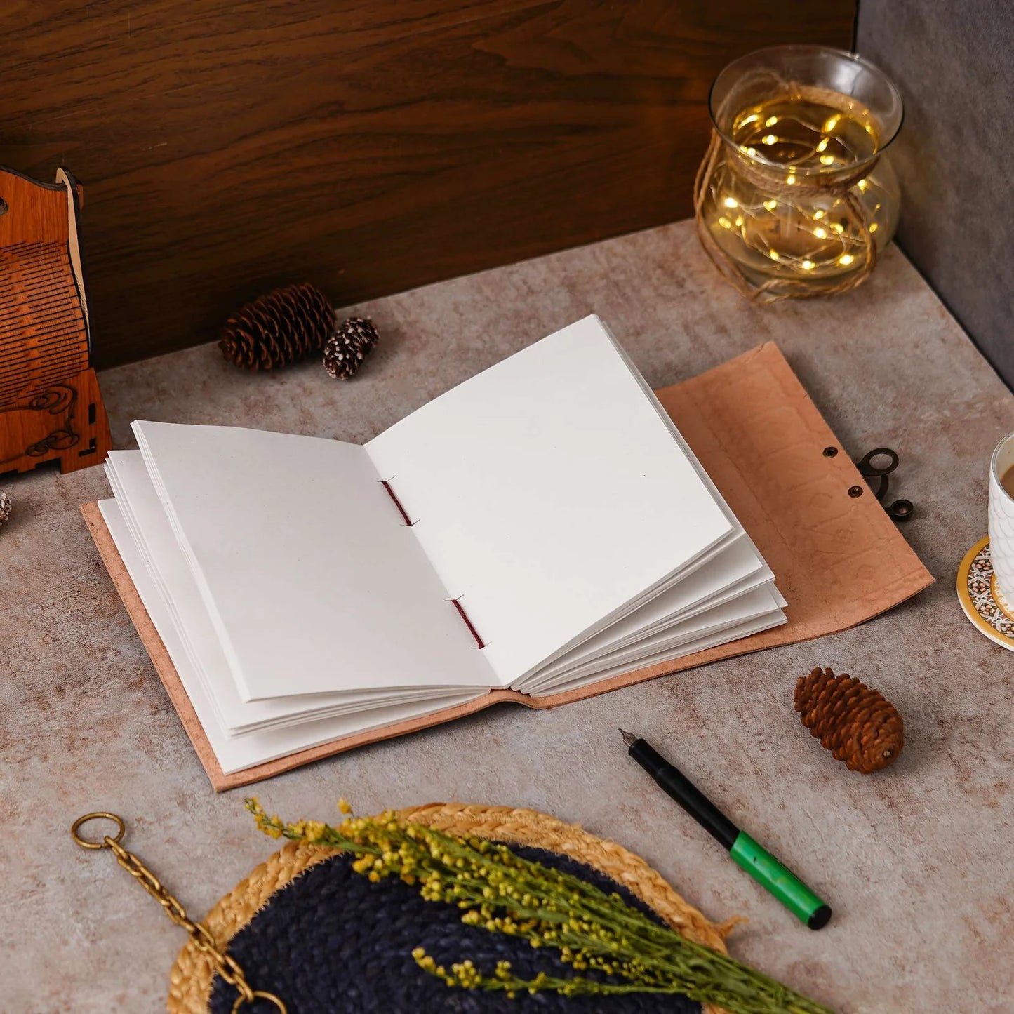 Open notebook on a textured surface with a pen, small plant, and decorative items.