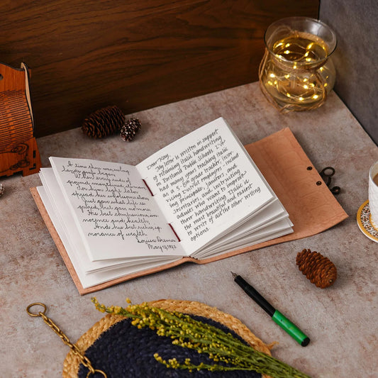 Open notebook on a textured surface with a pen, small plant, and decorative items.