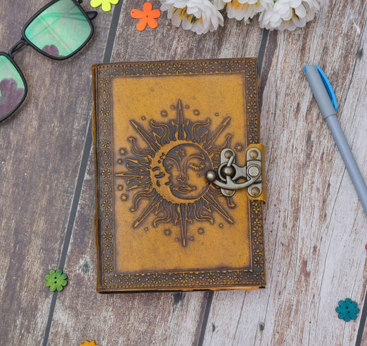Decorative notebook with sun and moon design on a wooden surface with flowers and a pen.