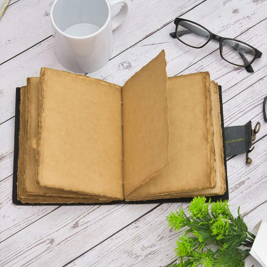 Open book on a wooden surface with a mug, glasses, and plant