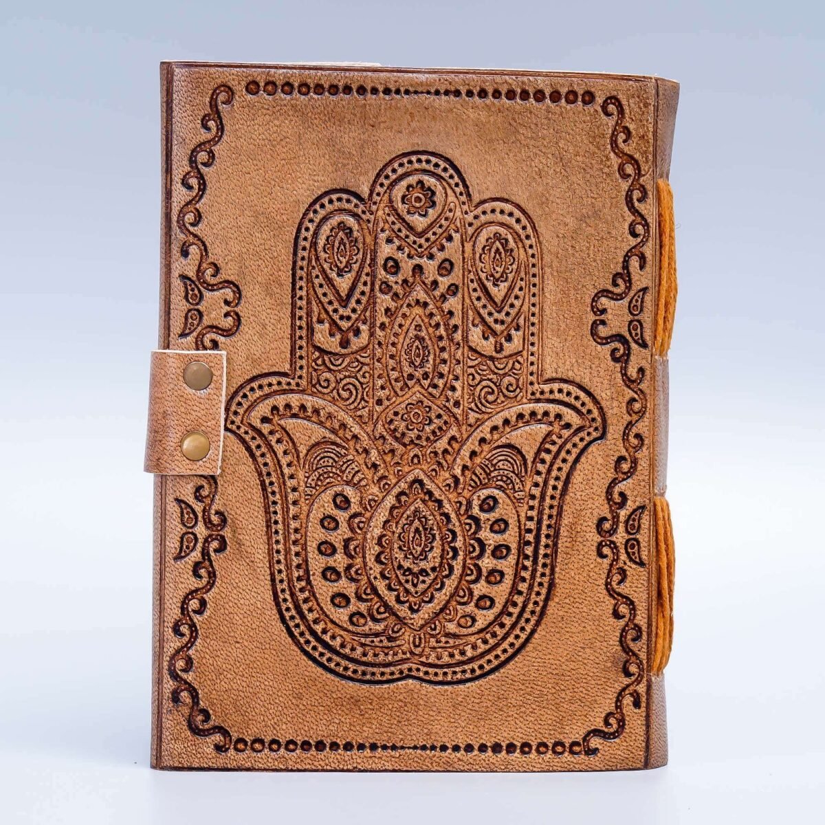 Brown leather notebook with Hamsa hand design on a light gray background