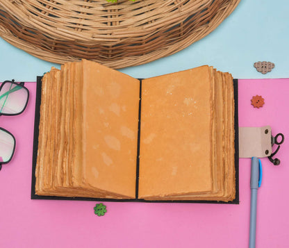 Open book with textured pages on a pink surface with decorative items.